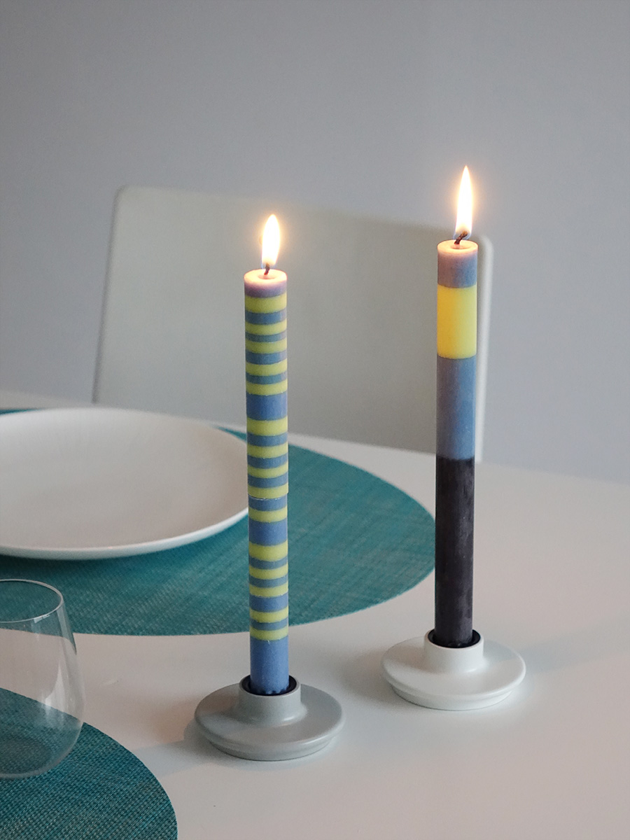 チルウィッチの楕円形のターコイズブルーのランチョンマットに合わせた水色と黄色ボーダーのキャンドルとライトグレイのテーパーキャンドルホルダーと水色・黄色・黒のボーダーのテーパーキャンドルとホワイトのキャンドルホルダーを組み合わせたテーブルコーディネート。