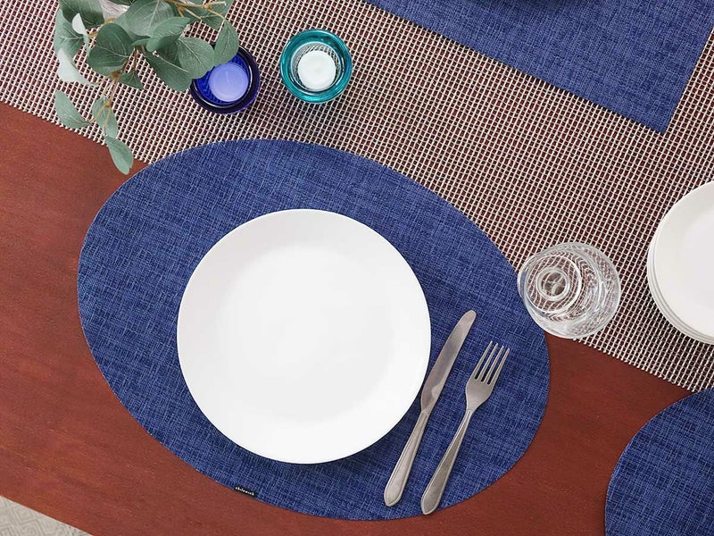 ダークブラウンの食卓に合わせた濃紺のレースの市松模様の楕円形のランチョンマットとシルバーのテーブルランナー　白の20cmプレートとシルバーのナイフとフォークとゴブレットを際立たせる楕円形のダークブルーのランチョンマット