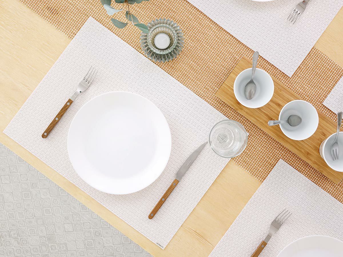 オークのテーブルにホワイトで多面体のテクスチャーのランチョンマットとざっくりした隙間のゴールドのテーブルランナーを合わせたコーディネート　白の23cmプレート皿と取っ手が木製のカトラリーを際立たせる白色のランチョンマット